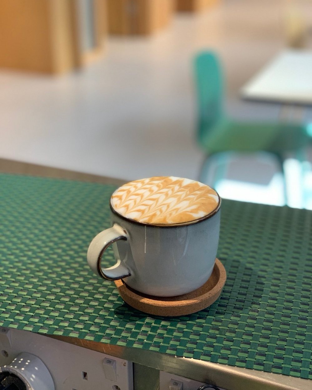 A flat white with rosetta latte art on a green woven table mat